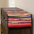 Colorful woven table runner on a wooden cabinet against a neutral wall.