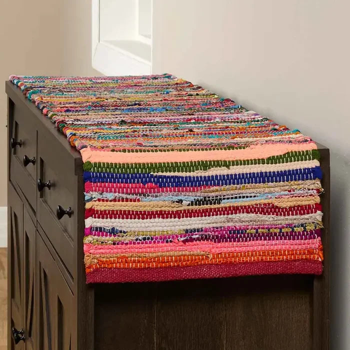 Colorful woven table runner on a wooden cabinet against a neutral wall.