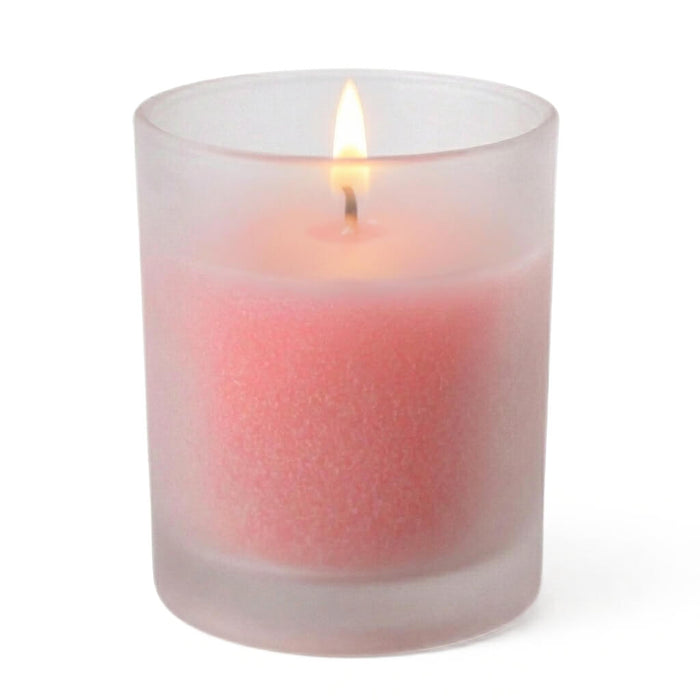 Lit pink votive candle in a frosted votive holder standing on a white backdrop