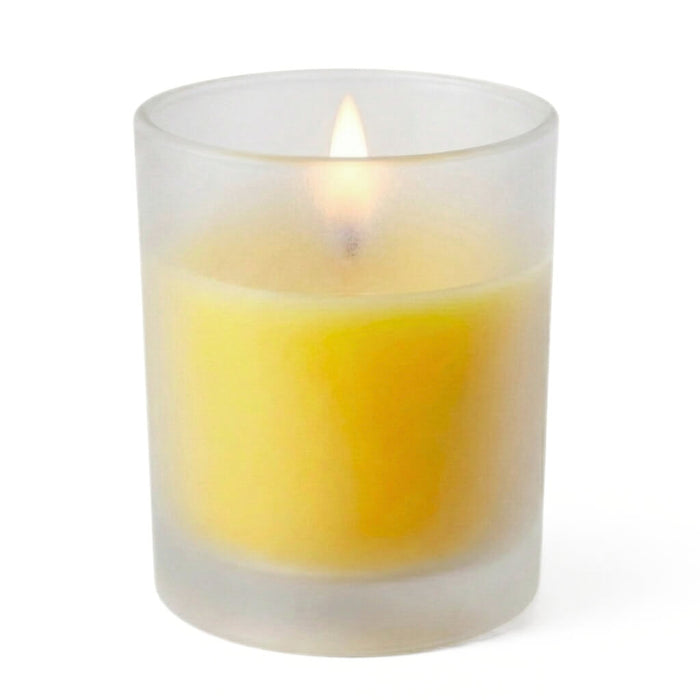 A lit yellow unscented candle inside a frosted votive holder on a solid white background