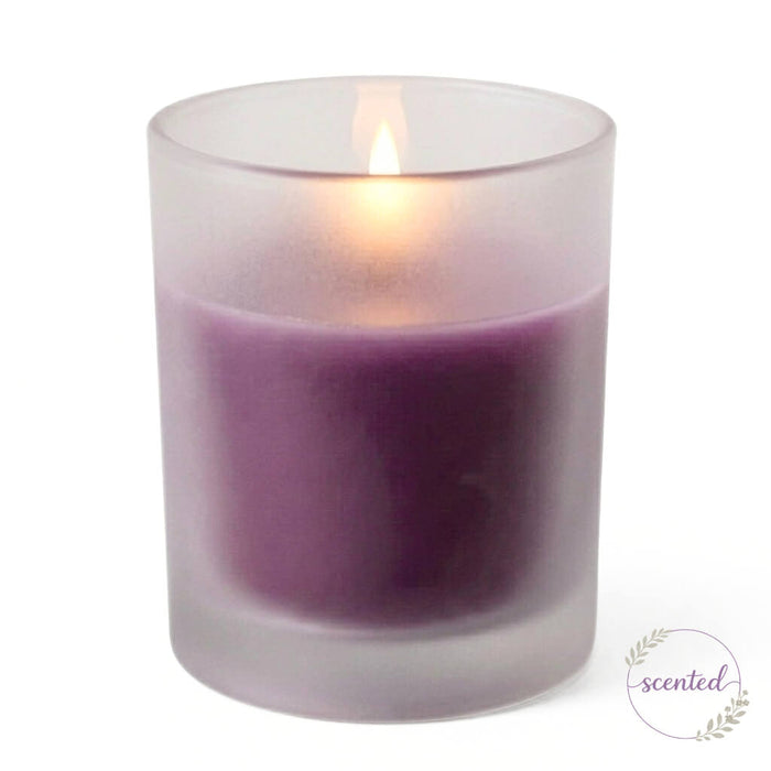 A single lit purple scented votive candle in a frosted glass holder