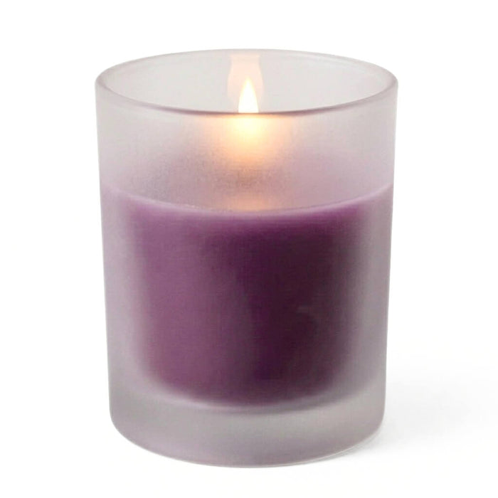Lit purple candle in a frosted glass holder on a white backdrop