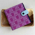 Purple wallet with white cat pattern on a wooden surface